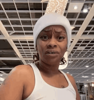 A Woman Wearing A White Beanie And A White Tank Top Is Making A Funny Face . GIF