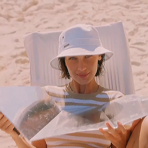 A Woman Wearing A White Bucket Hat And A Striped Shirt Is Smiling . GIF