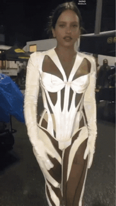 A Woman Wearing A White Corset And White Gloves Stands In Front Of A Blue Tarp GIF