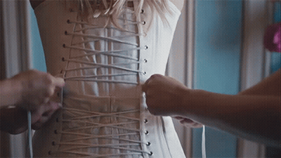 A Woman Wearing A White Corset Is Being Laced Up GIF