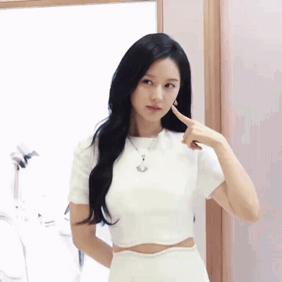 A Woman Wearing A White Crop Top And A White Skirt Is Pointing At Her Face . GIF