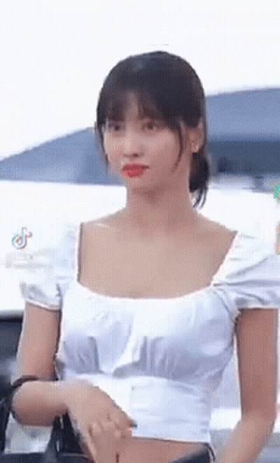 A Woman Wearing A White Crop Top Is Standing In Front Of A Car . GIF