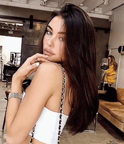A Woman Wearing A White Crop Top With A Gold Chain Shoulder Strap GIF