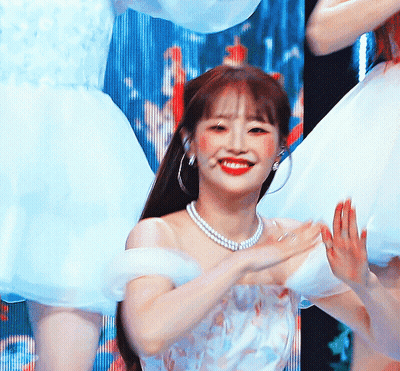A Woman Wearing A White Dress And A Pearl Necklace Smiles At The Camera GIF