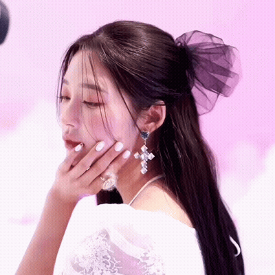 A Woman Wearing A White Dress And Earrings Has Her Hand On Her Chin GIF