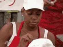 A Woman Wearing A White Hat And An Apron Is Eating A Sandwich . GIF