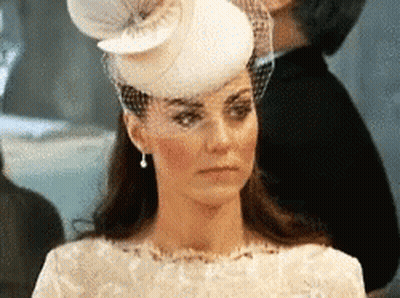 A Woman Wearing A White Hat And Veil Is Looking At The Camera . GIF