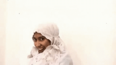 A Woman Wearing A White Hijab And A White Dress Is Smiling . GIF