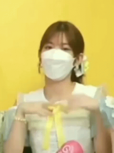 A Woman Wearing A White Mask Is Making A Heart Shape With Her Hands . GIF