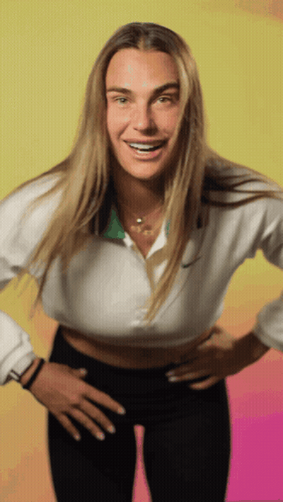 A Woman Wearing A White Nike Shirt And Black Pants Smiles With Her Hands On Her Hips GIF
