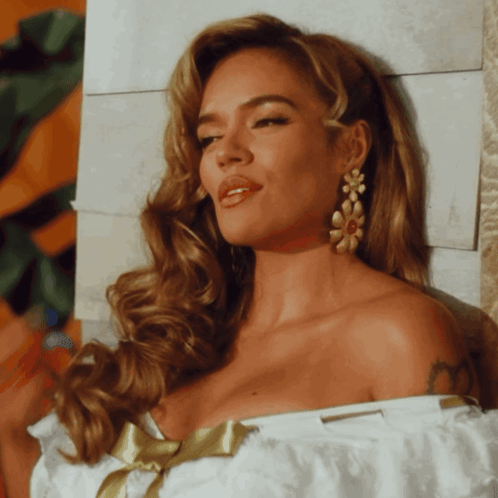 A Woman Wearing A White Off The Shoulder Top With A Gold Bow GIF