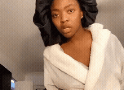 A Woman Wearing A White Robe And A Black Hat Is Making A Funny Face . GIF