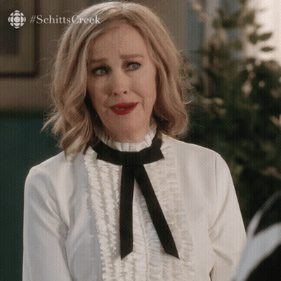 A Woman Wearing A White Shirt And A Black Bow Tie With #Schitts Creek On The Bottom GIF