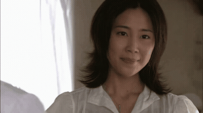 A Woman Wearing A White Shirt And A Necklace Looks At The Camera GIF