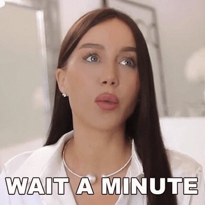 A Woman Wearing A White Shirt And A Necklace Says Wait A Minute . GIF