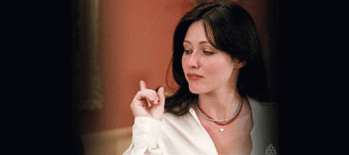 A Woman Wearing A White Shirt And A Necklace With A Heart On It GIF