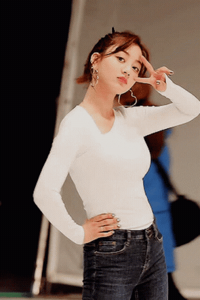 A Woman Wearing A White Shirt And Blue Jeans Is Giving A Peace Sign GIF