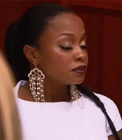 A Woman Wearing A White Shirt And Earrings Is Looking Down . GIF