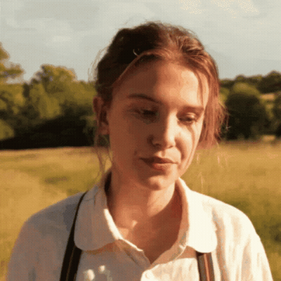 A Woman Wearing A White Shirt And Suspenders Looks Down GIF