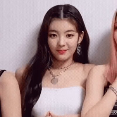 A Woman Wearing A White Strapless Top And A Necklace Is Standing Next To Two Other Women . GIF
