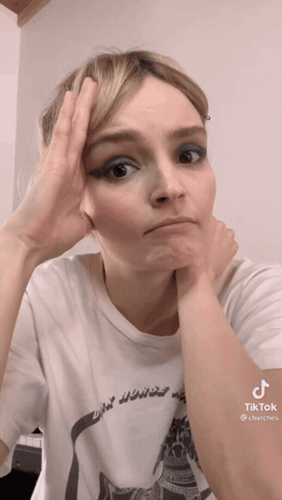 A Woman Wearing A White T-Shirt Has Her Hand On Her Forehead . GIF