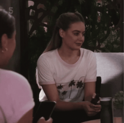 A Woman Wearing A White T-Shirt With Palm Trees On It Sits Next To Another Woman GIF