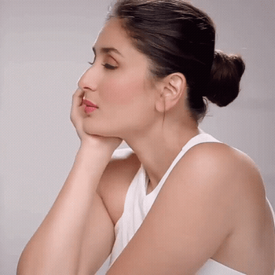 A Woman Wearing A White Tank Top Has Her Hand On Her Chin GIF