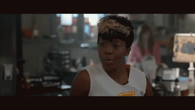 A Woman Wearing A White Tank Top With A Yellow Letter T On The Front GIF