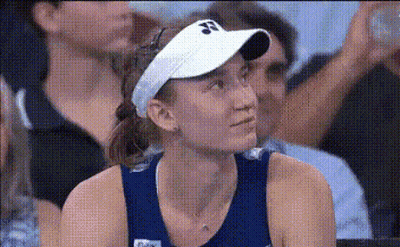 A Woman Wearing A White Visor Is Sitting In A Crowd . GIF