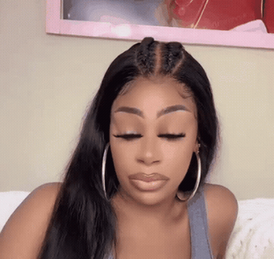 A Woman Wearing A Wig And Hoop Earrings Is Sitting On A Bed . GIF