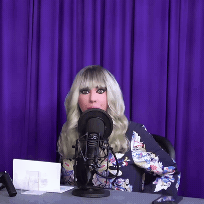 A Woman Wearing A Wig Is Sitting In Front Of A Microphone GIF