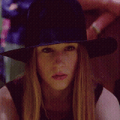 A Woman Wearing A Witch Hat Is Looking At The Camera GIF