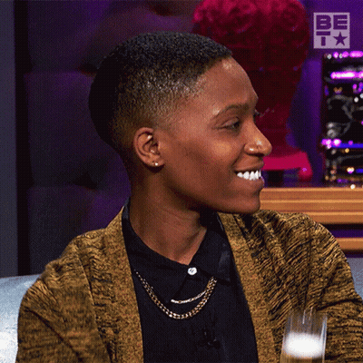 A Woman Wearing A Yellow Cardigan And A Black Shirt Is Smiling GIF