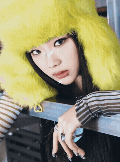 A Woman Wearing A Yellow Furry Hat And Striped Shirt GIF