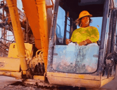 A Woman Wearing A Yellow Hard Hat Is Driving A Large Yellow Excavator GIF