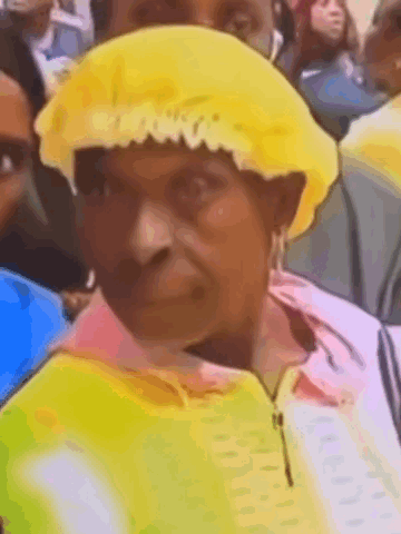 A Woman Wearing A Yellow Hat Is Sitting In A Crowd . GIF