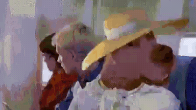 A Woman Wearing A Yellow Hat Is Sitting Next To A Man In A Suit On A Plane . GIF