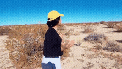 A Woman Wearing A Yellow Hat Is Standing In A Desert . GIF