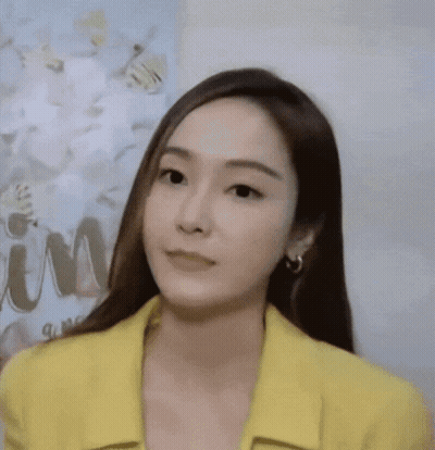 A Woman Wearing A Yellow Jacket And Earrings Is Looking At The Camera GIF