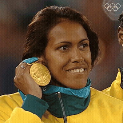 A Woman Wearing A Yellow Jacket Is Holding A Gold Medal Around Her Neck GIF