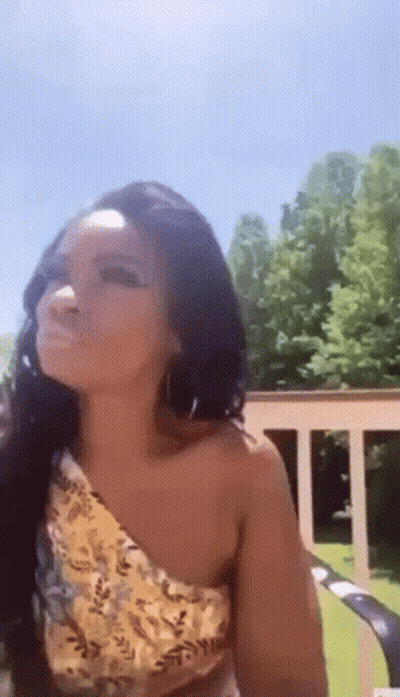 A Woman Wearing A Yellow One Shoulder Top And Earrings Is Sitting On A Lawn Chair . GIF