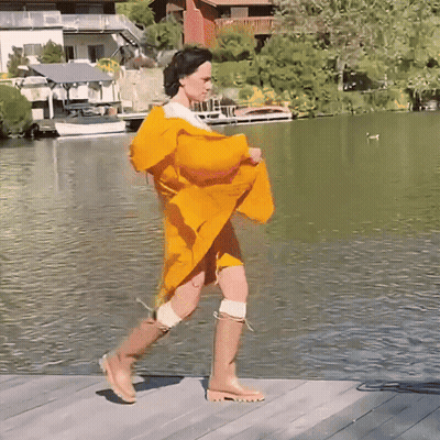 A Woman Wearing A Yellow Raincoat And Boots Is Walking By A Lake GIF