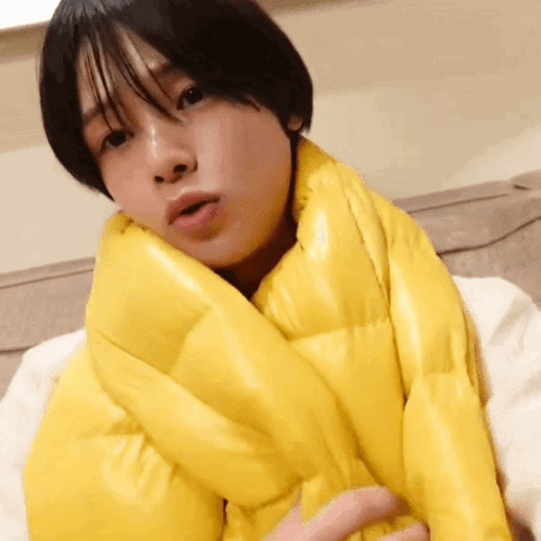 A Woman Wearing A Yellow Scarf Around Her Neck Looks At The Camera GIF