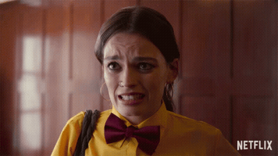 A Woman Wearing A Yellow Shirt And A Burgundy Bow Tie With A Netflix Logo In The Background GIF