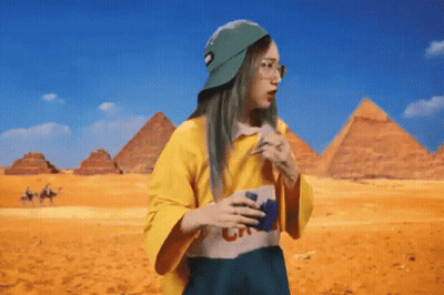 A Woman Wearing A Yellow Shirt And A Green Hat Is Standing In Front Of Pyramids . GIF