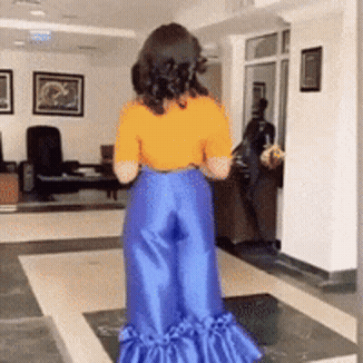 A Woman Wearing A Yellow Shirt And Blue Pants Is Standing In A Living Room GIF
