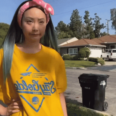 A Woman Wearing A Yellow Shirt That Says Golden State Warriors Is Standing Next To A Trash Can GIF