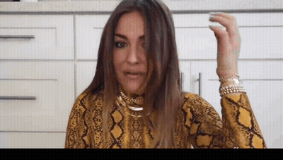 A Woman Wearing A Yellow Snake Print Shirt Is Holding Her Hair . GIF