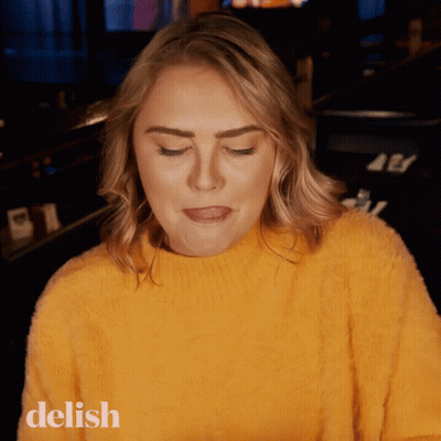 A Woman Wearing A Yellow Sweater With The Word Delish On The Bottom Left GIF