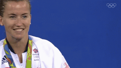 A Woman Wearing An Adidas Jacket Is Holding A Gold Medal In Front Of Her Face GIF